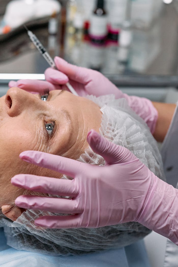 Close-up of a senior woman receiving a cosmetic injection in a clinical setting with gloves and a hairnet.